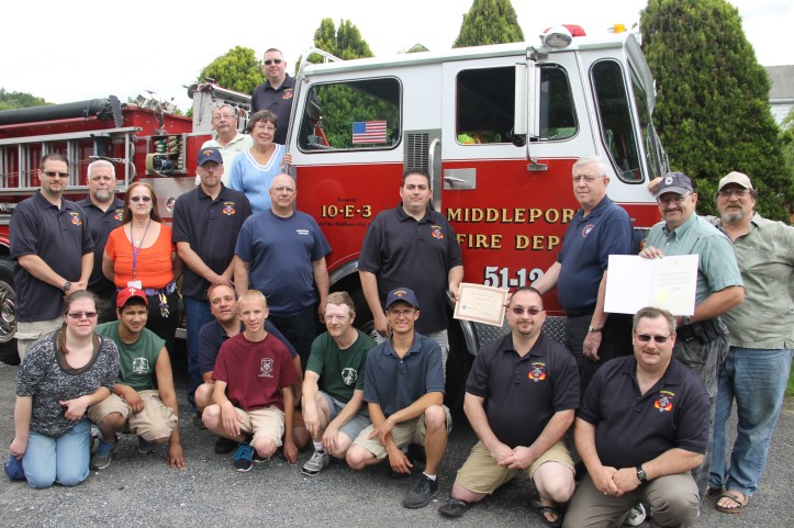 Pictured from front left are firefighters Vanessa Beach, fire police, Citizens Fire Company (CFC), Middleport PA; Tom Reynolds, CFC; Kevin Czaja, Middleport Fire Department (MFD) of Middleport NY; Justin Czaja, MFD; Todd Amos, Assistant Chief, CFC; Ryan Czaja, MFD; EMT Chad Fuller, MFD; and Dave Greenwell, past Chief MFD. Second row from left are firefighters Darren Burdick, Vice President, MFD; Ross Hageman, President, MFD; Scott Kassmann, trustee, MFD; Jim Volkosh, past chief, MFD; Nick Boyle, Chief, MFD; PA State Commissioner Ed Mann; Russell Hauck, CFC; and James Johnson, CFC. On truck are Bob Kester, MFD; Gail Kester, MFD; and Regan Ginty, MFD.