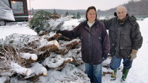 Dan and Cindy Schroeder stand next to snow-covered trees awaiting pickup by needy families.