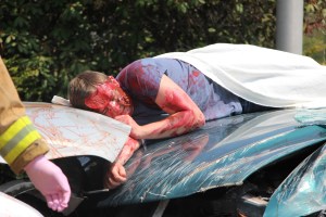 Covered half-way with a blanket on the hood of a car, James Kolbush portrays himself as a victim during mock DUI drill. Schuylkill County Deputy Coroner Taking part in the drill, David Truskowsky arrived and placed Kolbush in a body bag and the back of his vehicle.